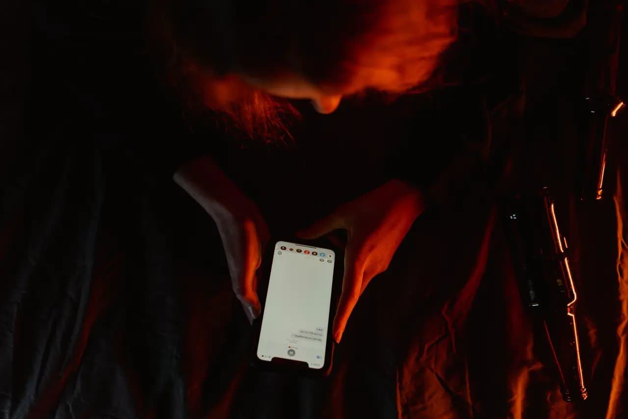 A person reading a message on their phone in a dimly lit room — illustrative stock photo